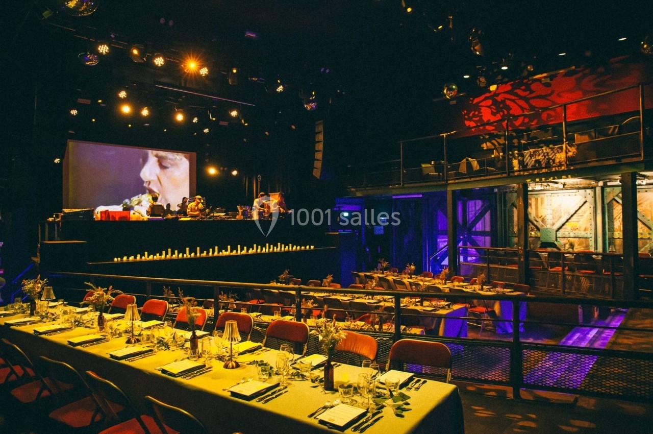 Salle de spectacle avec tables dressées, scène éclairée et écran projetant une image en arrière-plan.