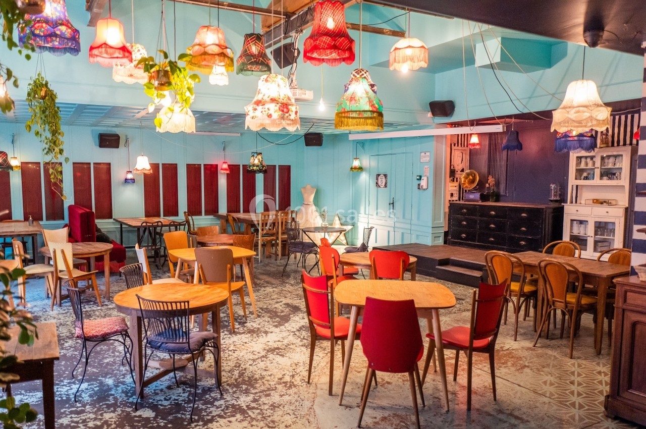 Salle colorée avec des tables en bois, chaises variées et des lampes suspendues décoratives dans un décor éclectique.