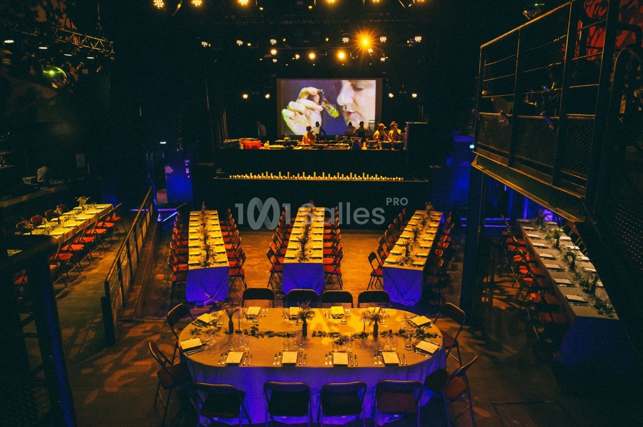 Salle de réception avec tables dressées, éclairage tamisé et écran géant en arrière-plan.