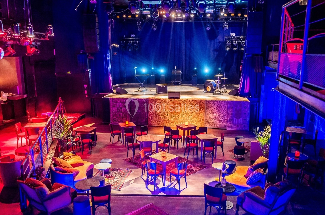 Salle de concert vide avec scène éclairée, instruments de musique et tables disposées dans un espace chaleureux.