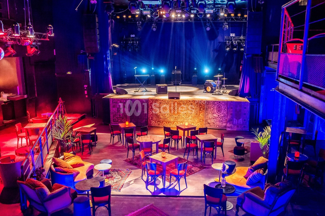 Salle de concert vide avec scène éclairée, instruments de musique et tables disposées dans un espace chaleureux.