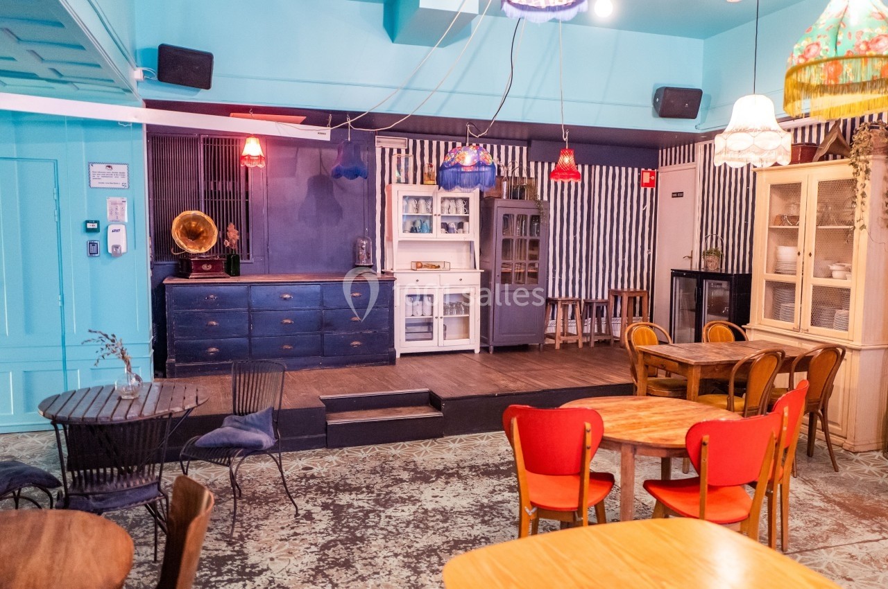 Salle de café colorée avec mobilier éclectique, lampes suspendues et un comptoir rétro en arrière-plan.