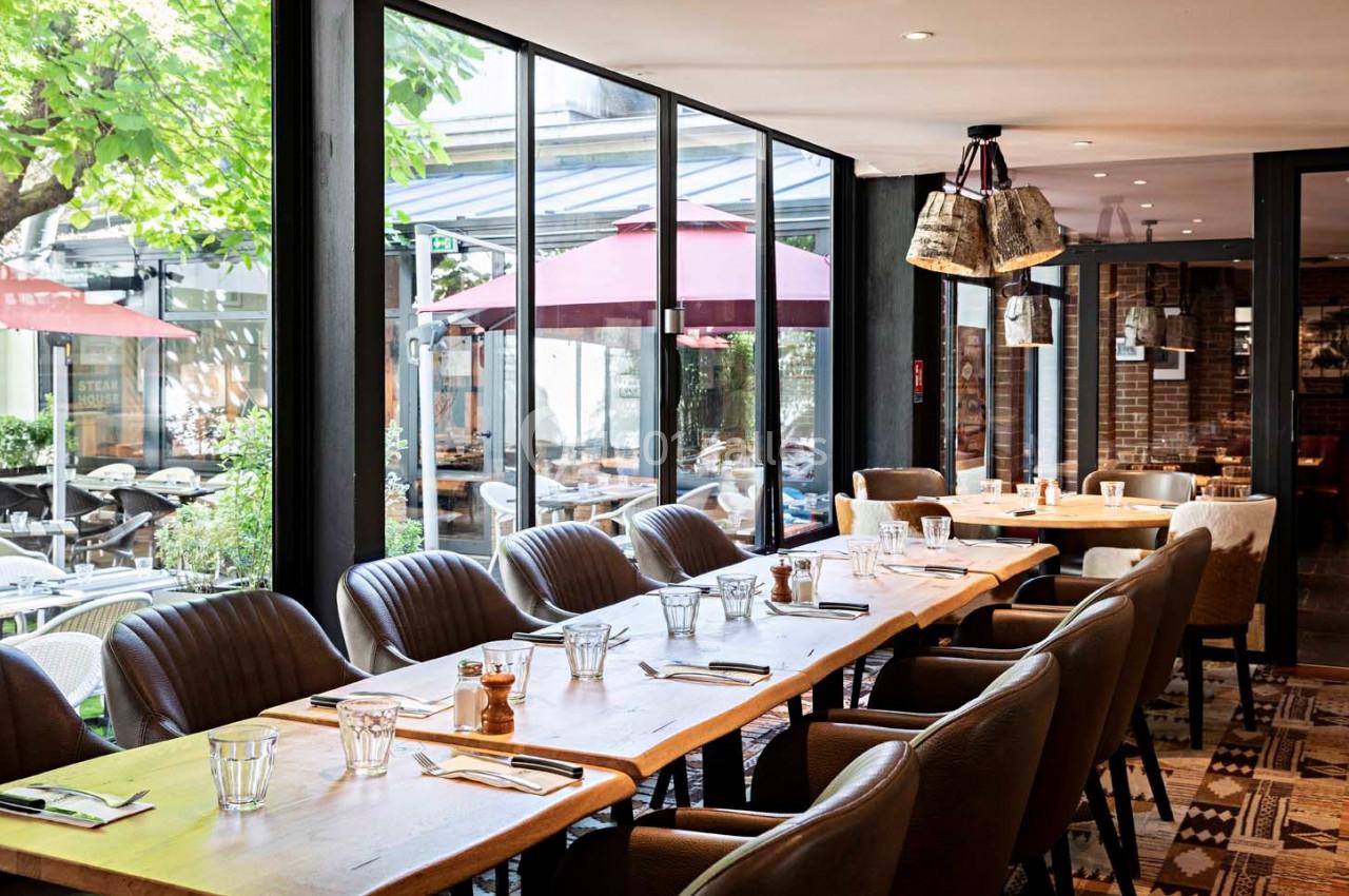 Salle de restaurant lumineuse avec de grandes baies vitrées donnant sur une terrasse équipée de parasols rouges.