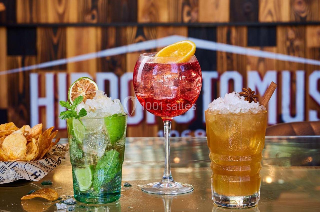 Trois cocktails colorés garnis de fruits et d'herbes, posés sur un comptoir avec des chips en arrière-plan.