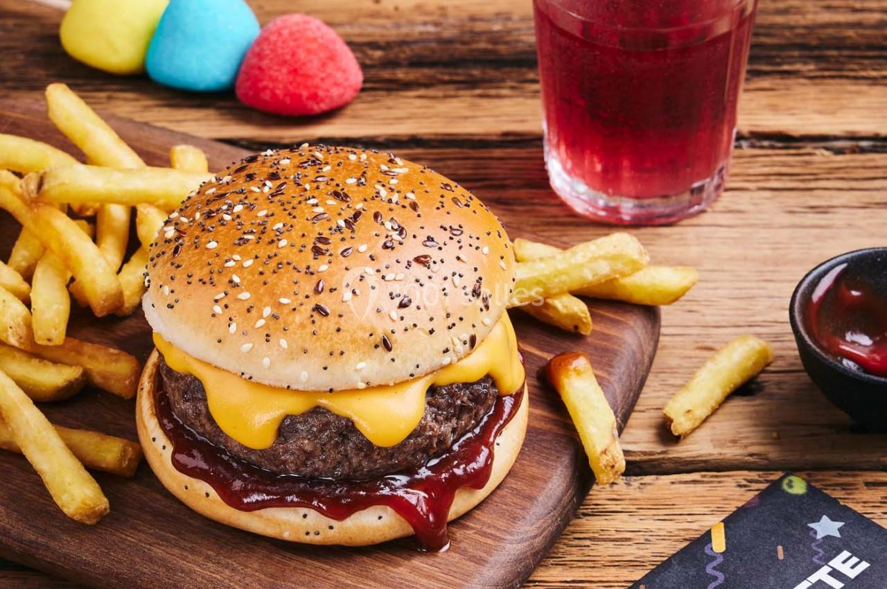 Burger au fromage avec sauce barbecue, accompagné de frites, sur une planche en bois, avec une boisson et des bonbons…