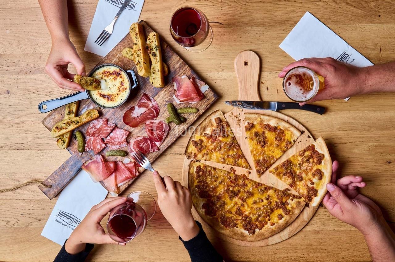 Repas convivial avec planche de charcuterie, fromage fondu, cornichons et pizza, accompagné de verres de vin et de bière.