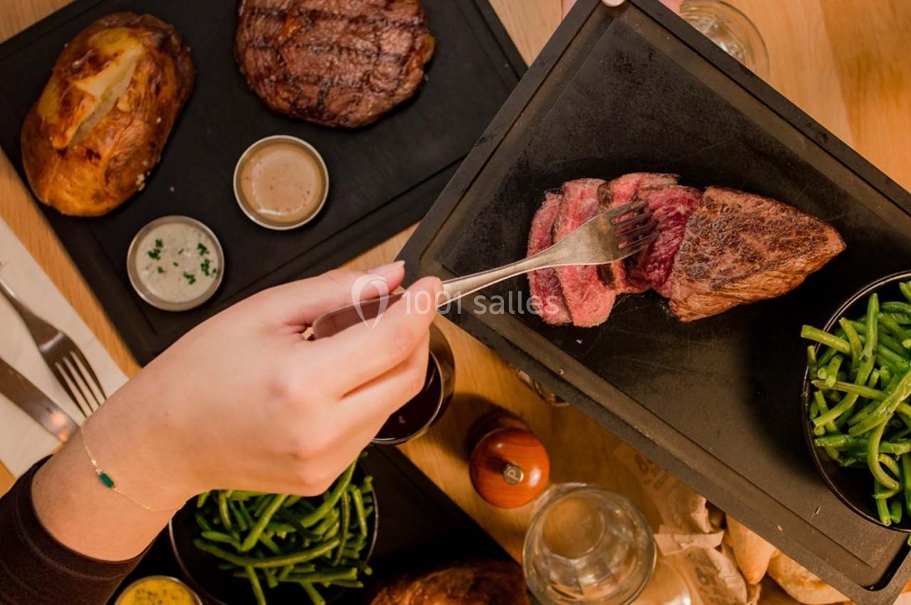 Une personne coupe un morceau de viande saignante sur une planche, accompagnée de haricots verts et d'autres plats.