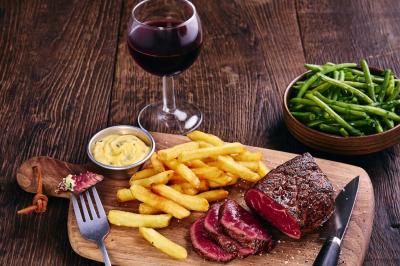 Miniature Location salle Boulogne-Billancourt (Hauts-de-Seine) - Hippopotamus Boulogne #27 Plat de viande rouge tranchée avec sauce au poivre, accompagné de frites, servi dans un plat ovale sur une table en bois.