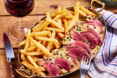 Miniature Location salle Boulogne-Billancourt (Hauts-de-Seine) - Hippopotamus Boulogne #29 Plat de viande rouge tranchée avec sauce au poivre, accompagné de frites, servi dans un plat ovale sur une table en bois.