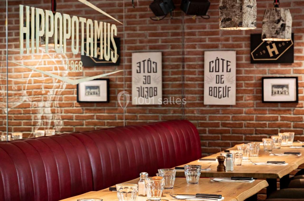 Salle de restaurant avec banquettes rouges, tables en bois dressées et murs en briques décorés d'affiches.