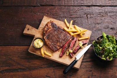Plat de viande rouge tranchée avec sauce au poivre, accompagné de frites, servi sur un plateau avec un verre de vin rouge.