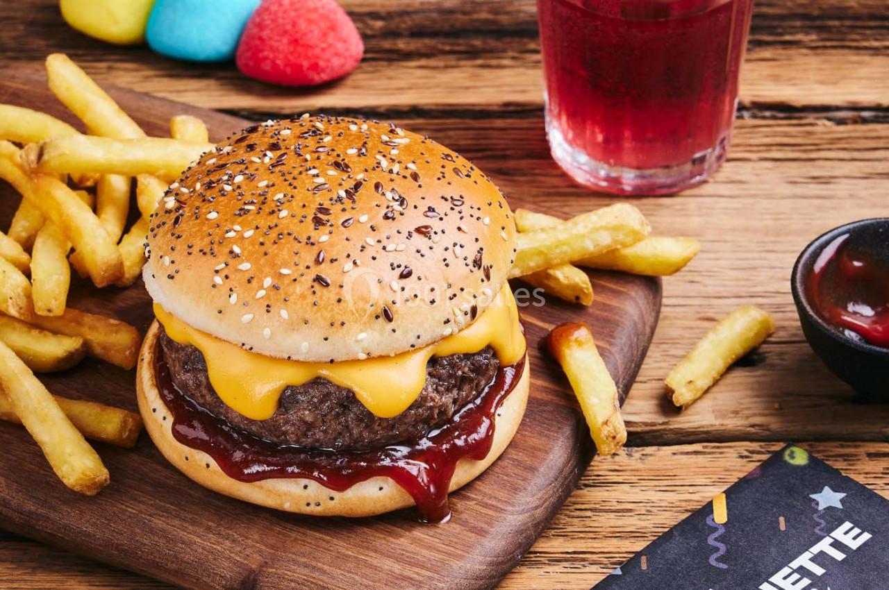 Burger au fromage avec sauce barbecue, accompagné de frites, sur une planche en bois avec un verre de boisson rouge.