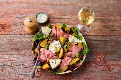 Plat de viande rouge tranchée avec sauce au poivre, accompagné de frites, servi sur un plateau avec un verre de vin rouge.