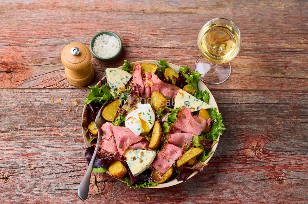 Assiette de salade composée avec rosbif, pommes de terre rôties, fromage bleu et herbes, accompagnée de vin blanc.