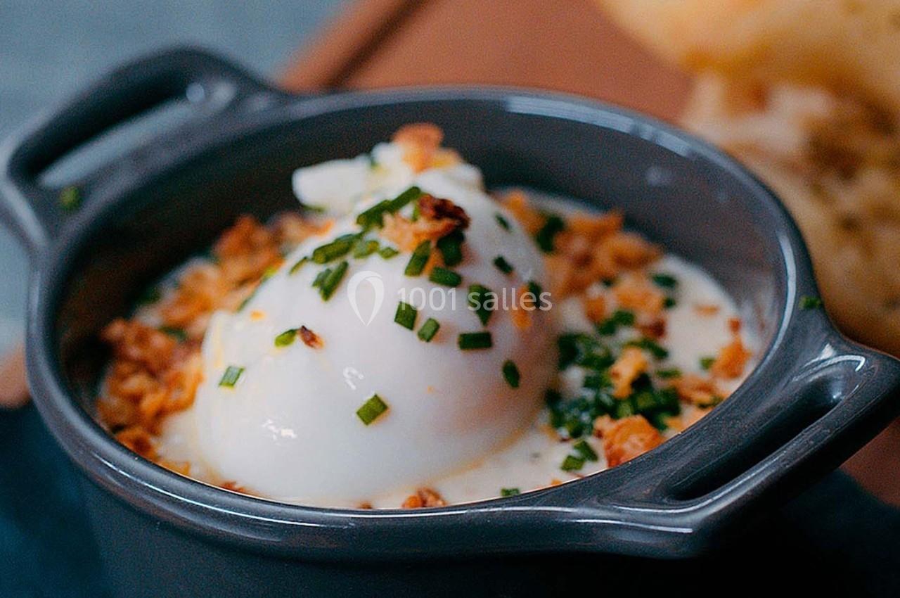 Oeuf poché servi dans une petite cocotte avec une garniture de ciboulette et d'oignons croustillants.