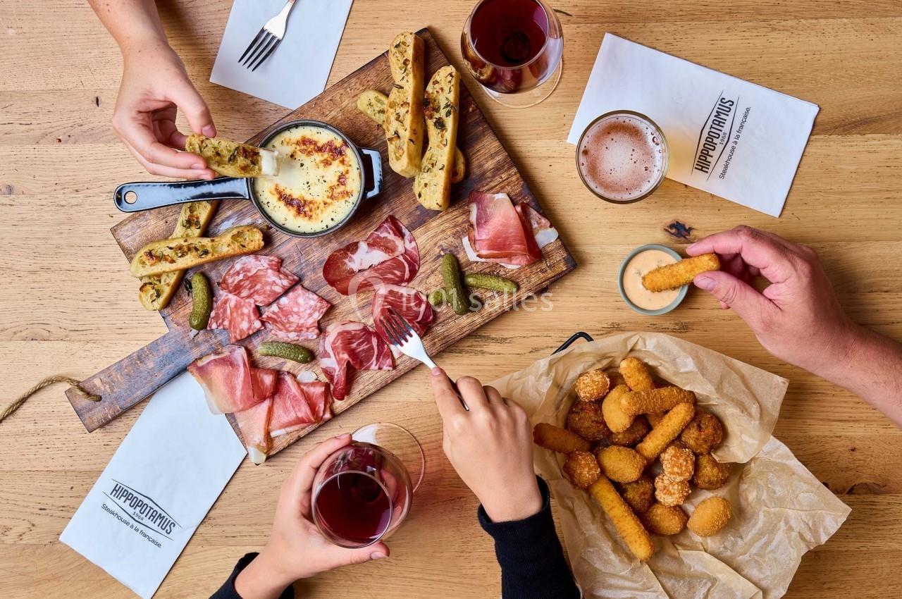 Planche de charcuterie avec fromage fondu, cornichons, gressins et boissons sur une table en bois.