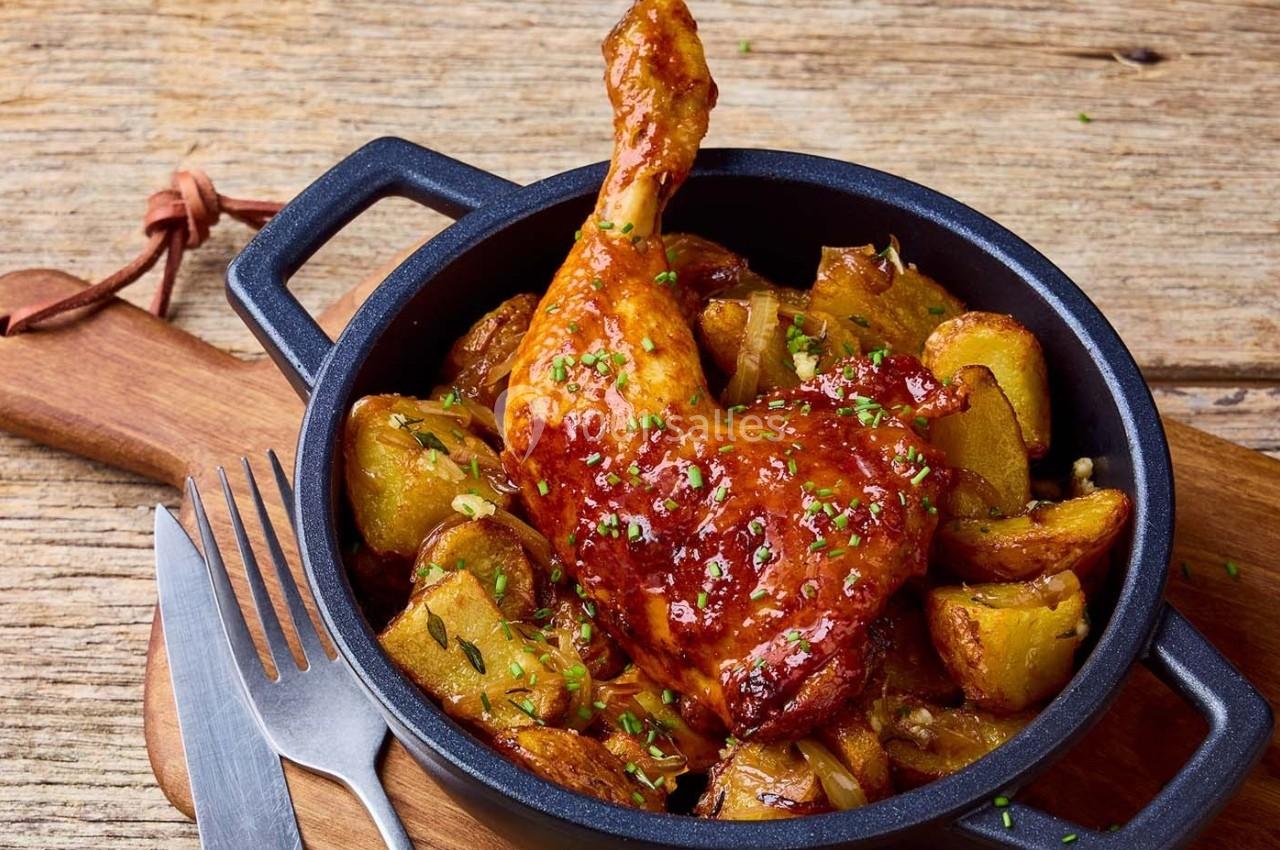 Cuisse de poulet rôtie avec pommes de terre dorées, servie dans une poêle en fonte sur une table en bois.