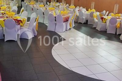 Salle de réception décorée avec des tables rondes dressées de nappes jaunes et rouges, chaises blanches et lustres suspendus.
