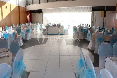 Salle de réception décorée avec des tables rondes dressées de nappes jaunes et rouges, chaises blanches et lustres suspendus.