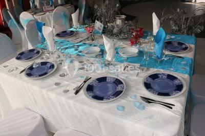 Salle de réception décorée avec des tables rondes dressées de nappes jaunes et rouges, chaises blanches et lustres suspendus.