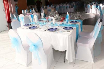 Salle de réception décorée avec des tables rondes dressées de nappes jaunes et rouges, chaises blanches et lustres suspendus.