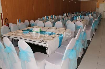 Salle de réception décorée avec des tables rondes dressées de nappes jaunes et rouges, chaises blanches et lustres suspendus.