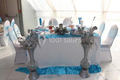 Salle de réception décorée avec des tables rondes dressées de nappes jaunes et rouges, chaises blanches et lustres suspendus.