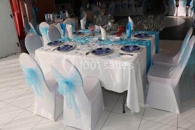 Salle de réception décorée avec des tables rondes dressées de nappes jaunes et rouges, chaises blanches et lustres suspendus.