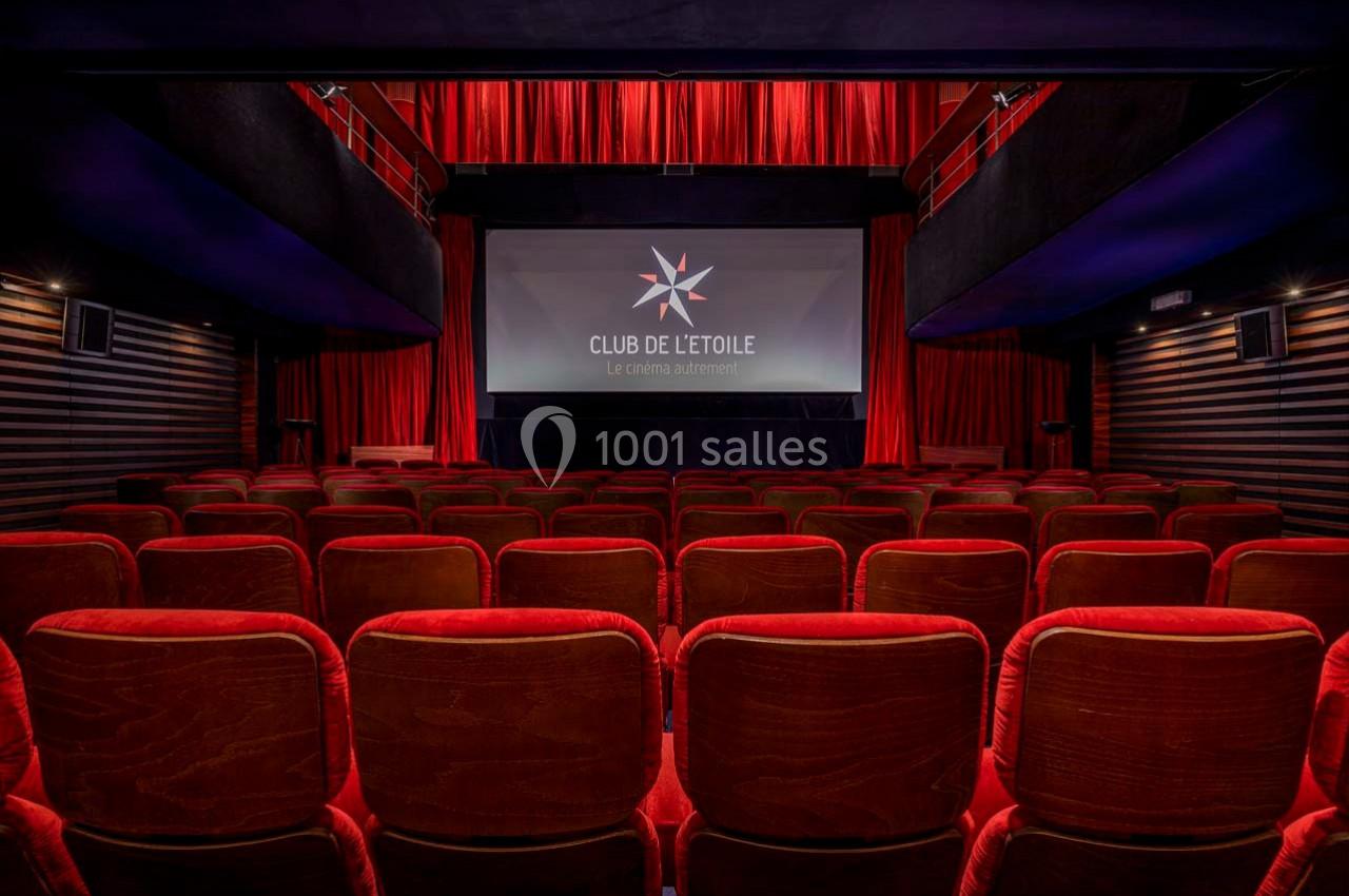 Salle de cinéma vide avec des fauteuils rouges, un écran allumé affichant un logo et des rideaux rouges en arrière-plan.