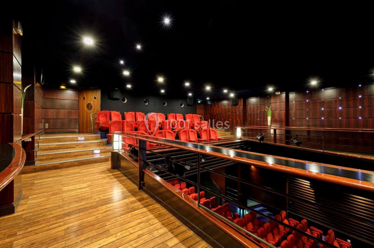 Salle de cinéma avec sièges rouges, parquet en bois et éclairage tamisé dans un décor moderne.