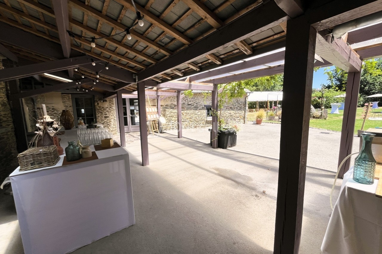 Espace extérieur couvert avec tables décorées, murs en pierre et vue sur une cour ensoleillée.