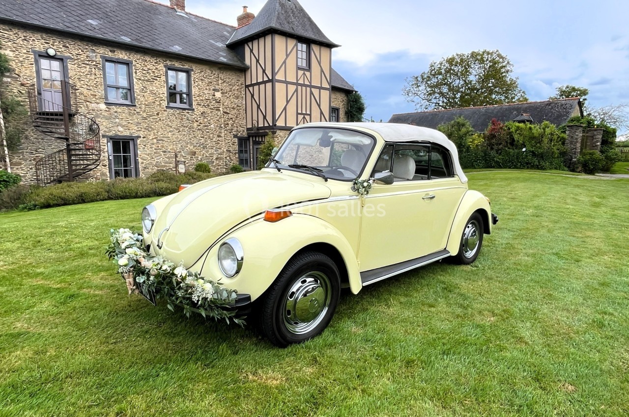 Voiture ancienne décapotable jaune ornée de fleurs, stationnée sur une pelouse devant une maison en pierre et colombages.