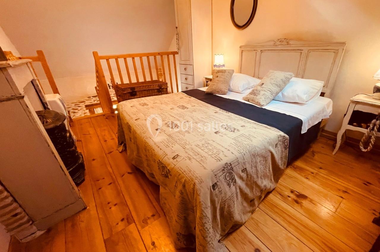 Chambre avec lit double, parquet en bois, mobilier ancien et lumière douce dans un espace mansardé.