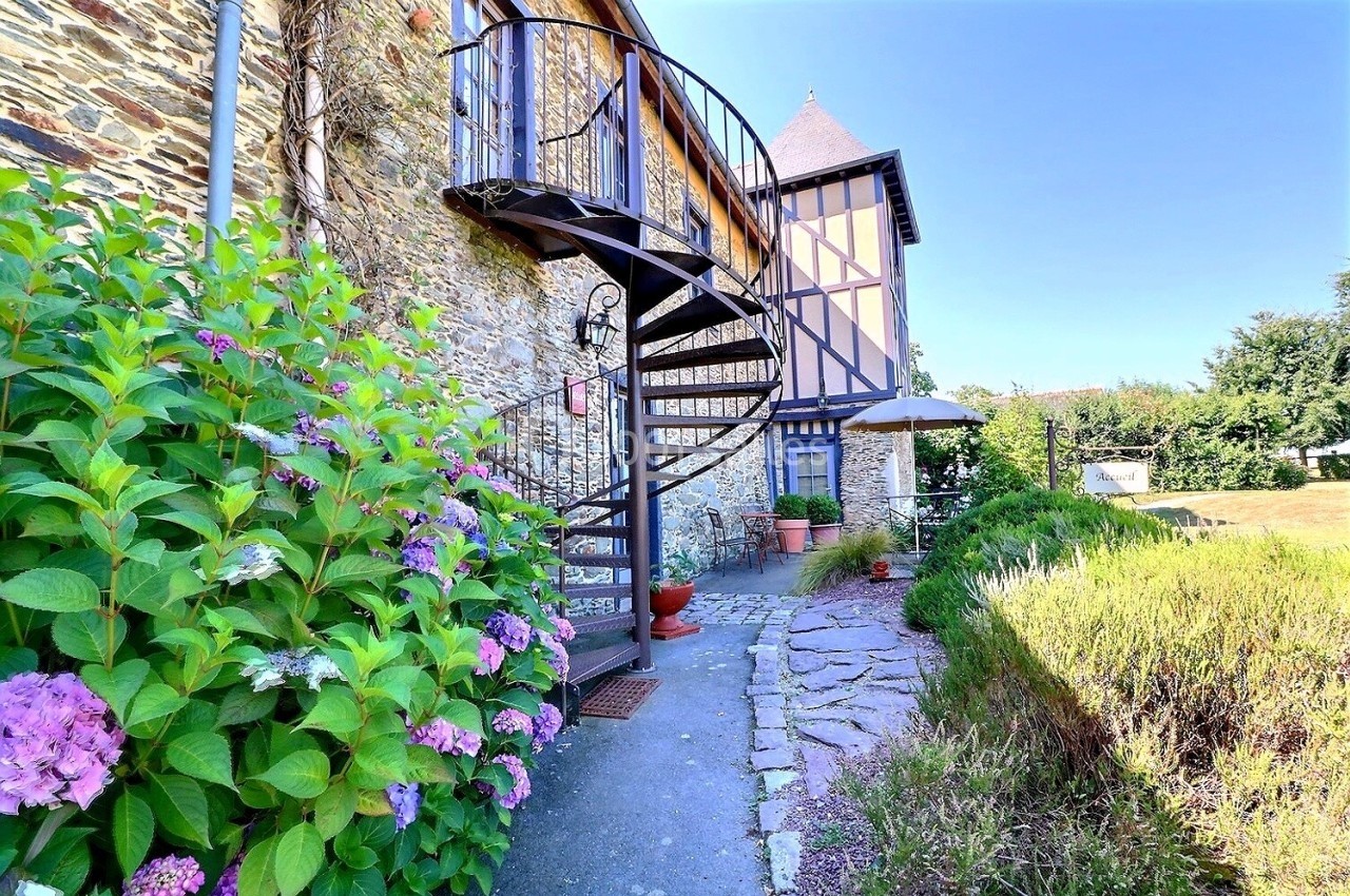 Escalier en colimaçon extérieur en métal longeant un mur en pierre, entouré de fleurs et d'un jardin.