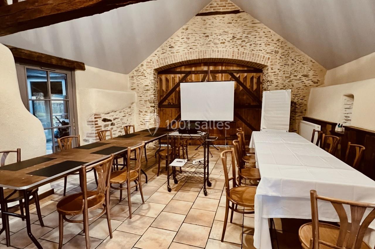 Salle rustique avec poutres apparentes, tables et chaises en bois disposées pour une réunion ou un événement.