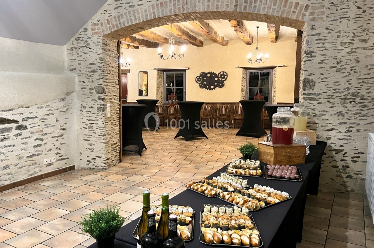 Salle en pierre avec tables dressées pour un buffet, comprenant boissons, verrines et amuse-bouches.