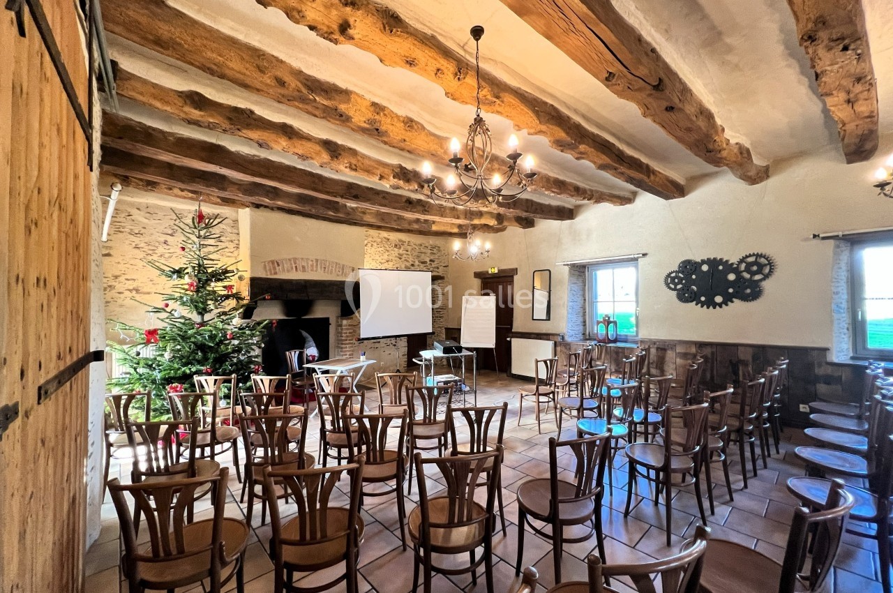 Salle de réunion rustique avec poutres apparentes, chaises en bois, sapin décoré et équipements de présentation.