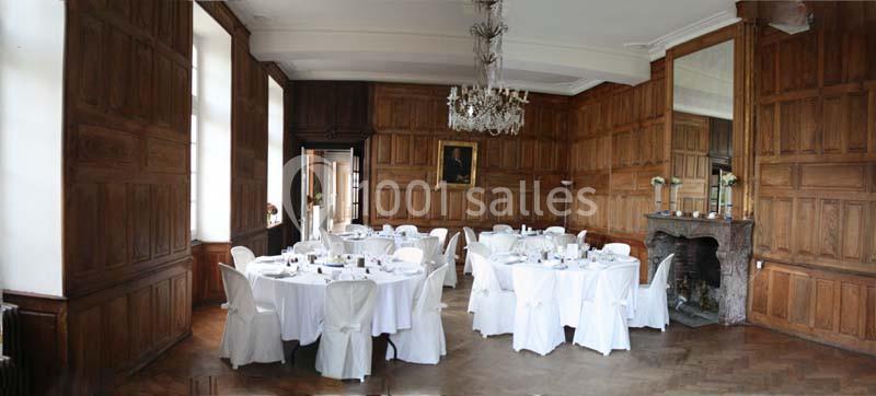 Salle à manger élégante avec murs en boiseries, tables rondes dressées et cheminée ornée d'un miroir.