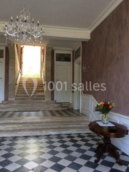Hall d'entrée avec escalier en pierre, sol en damier noir et blanc, table en bois et bouquet de fleurs.