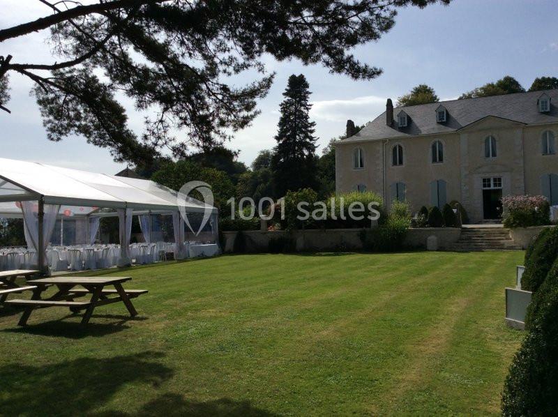 Jardin avec pelouse bien entretenue, grande tente blanche aménagée et maison en arrière-plan sous un ciel dégagé.