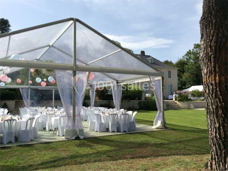 Tente transparente installée sur une pelouse, aménagée avec des tables et chaises blanches pour un événement en plein air.