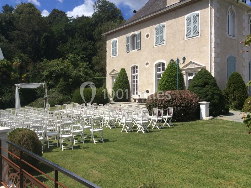 Chaises blanches disposées en rangées sur une pelouse devant une grande maison, préparées pour une cérémonie en extérieur.