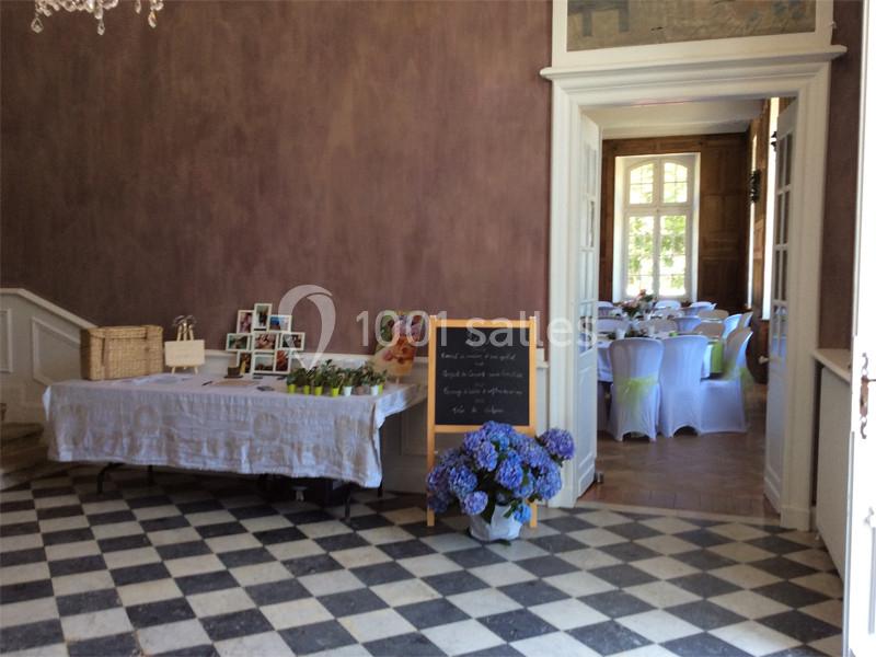 Table avec décorations et ardoise dans une entrée, donnant sur une salle aménagée avec des tables dressées.