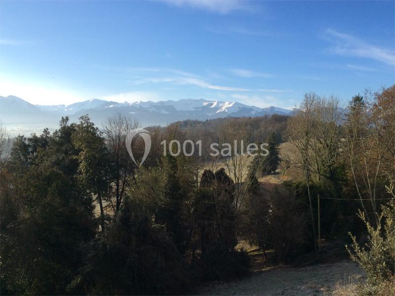 Paysage rural avec des arbres, collines et montagnes enneigées sous un ciel bleu dégagé.