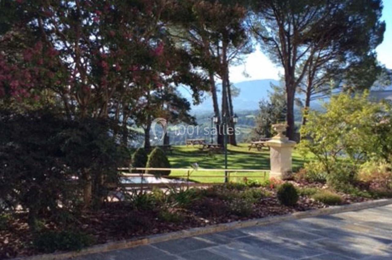 Vue d'un jardin arboré avec pelouse, bancs en bois et montagnes en arrière-plan sous un ciel dégagé.