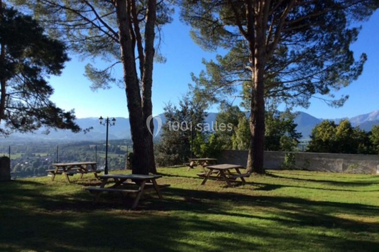 Tables de pique-nique en bois disposées sur une pelouse ombragée, avec vue sur des montagnes et un ciel dégagé.