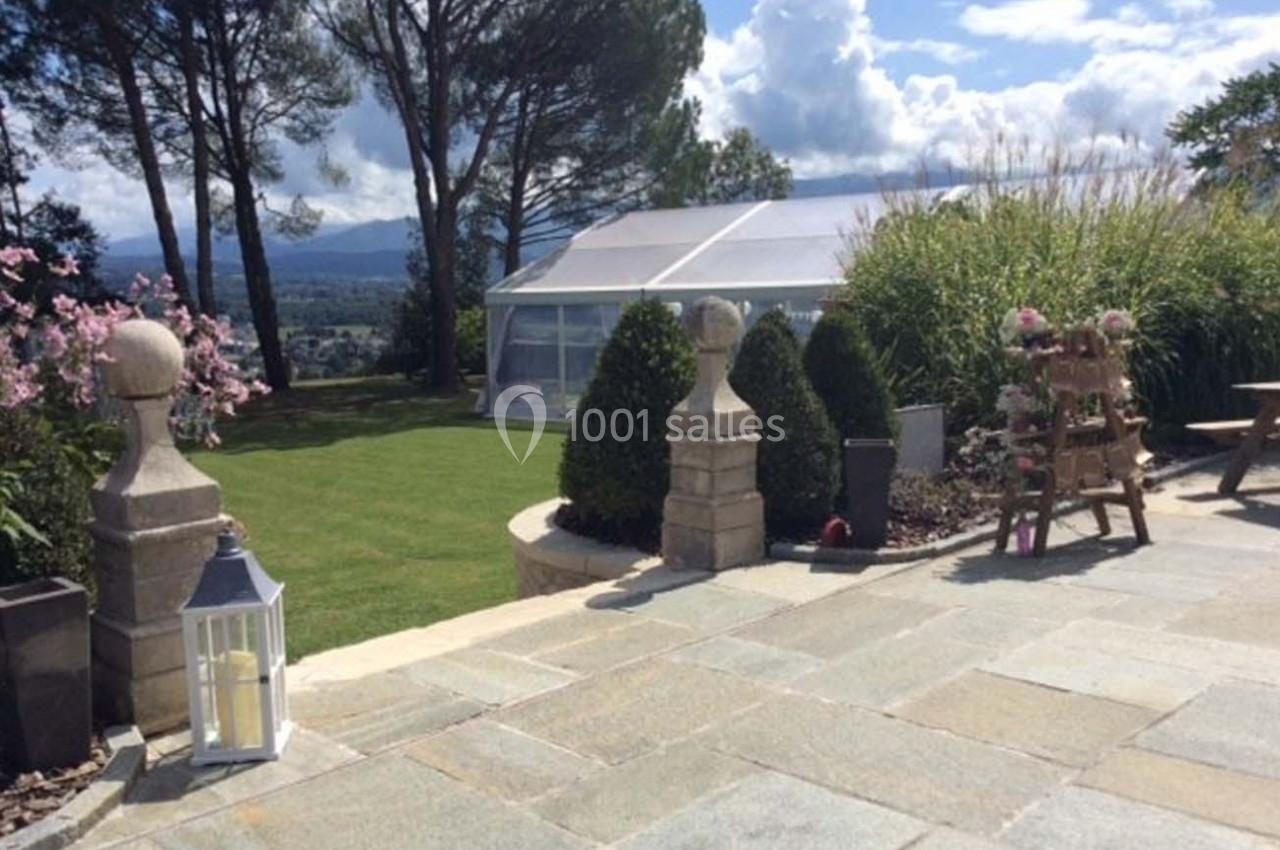 Terrasse en pierre avec vue sur un jardin verdoyant, des arbres et une structure transparente au fond.