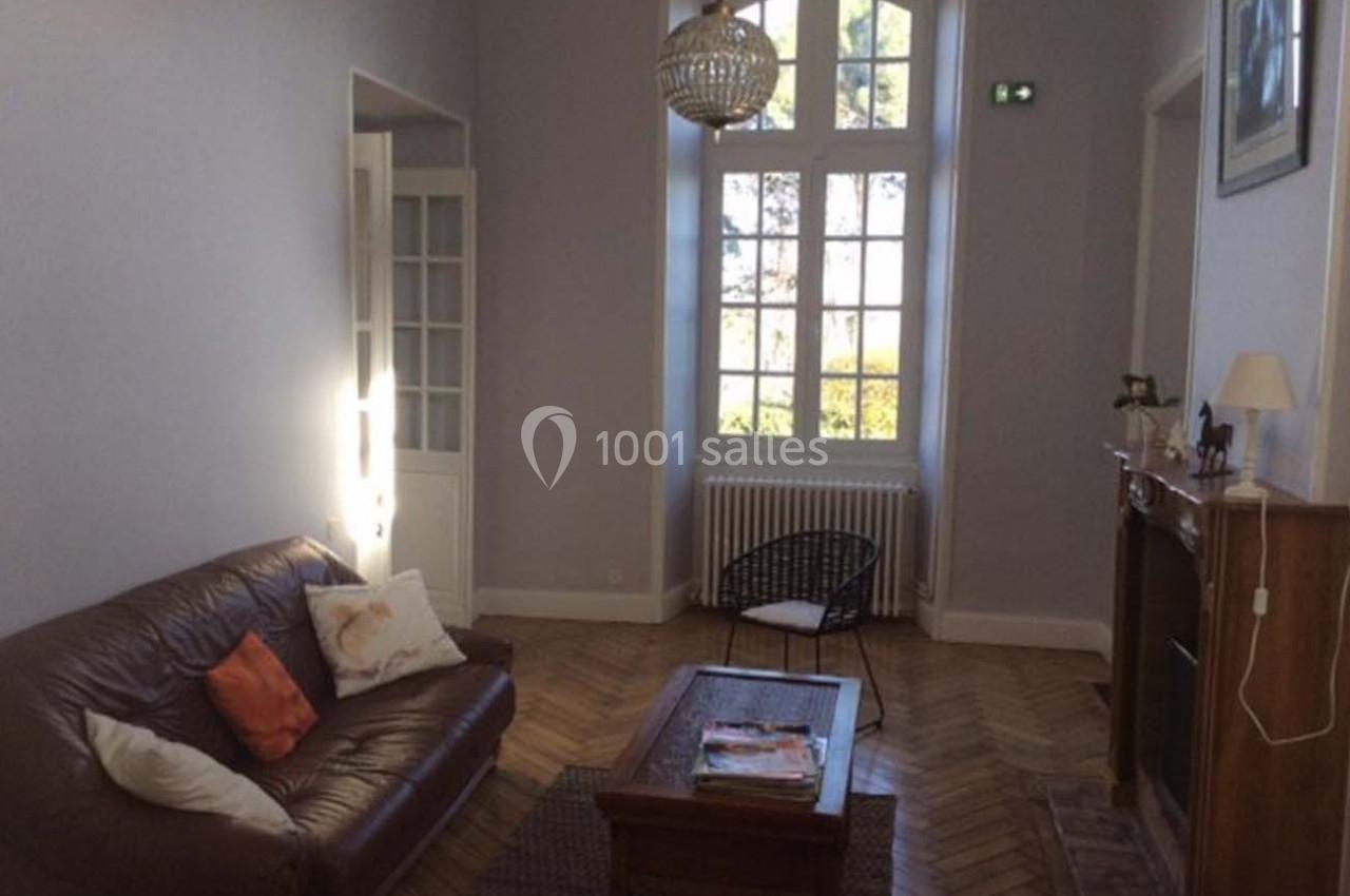 Salon lumineux avec canapé en cuir, table basse en bois, cheminée et grande fenêtre donnant sur un jardin.