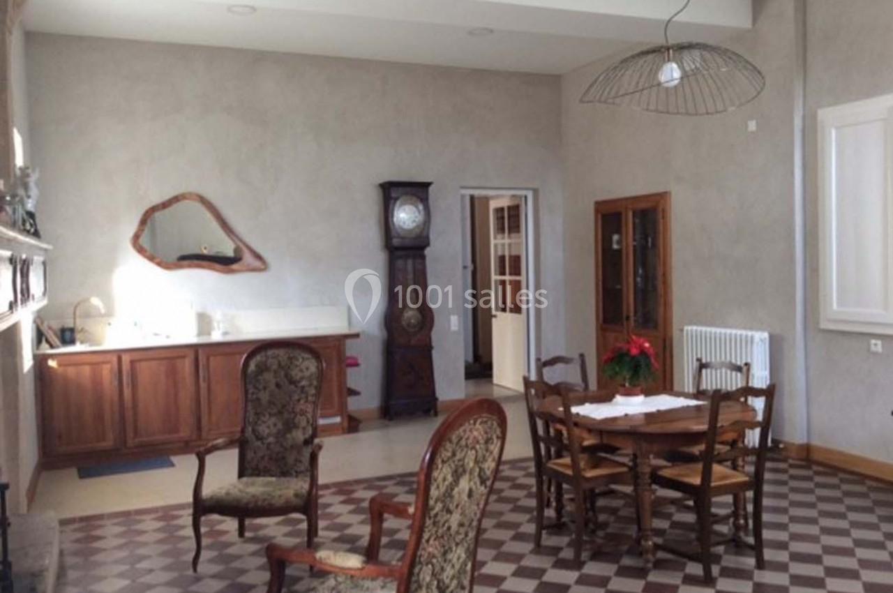 Salle à manger lumineuse avec table en bois, chaises assorties, horloge ancienne et sol en carreaux bicolores.