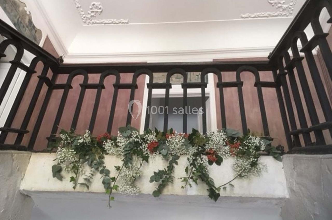 Guirlande de feuillage et fleurs blanches et rouges suspendue à une rambarde en bois dans un intérieur lumineux.